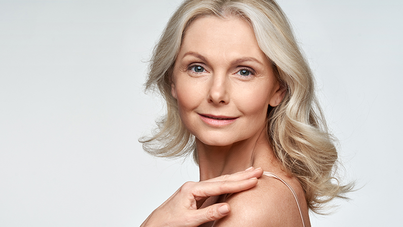 Attractive gorgeous mature older woman looking at camera isolated on white background advertising skincare spa treatment. Mid age tightening face skin care rejuvenation cosmetics concept. Portrait